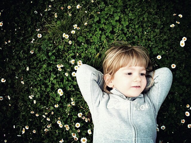 A young girl relaxing in a patch of clover and daisies.